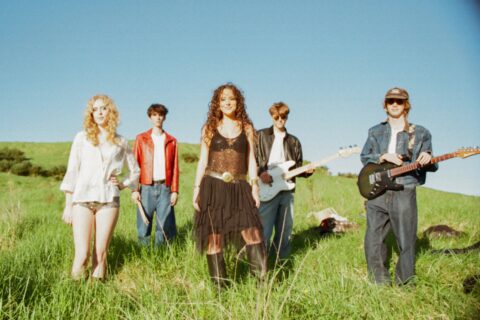 5 band members of Where's Jai standing in long green grass holding instruments