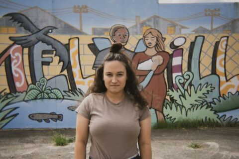 Cian stands in front of a wall with street art that says "Melville"