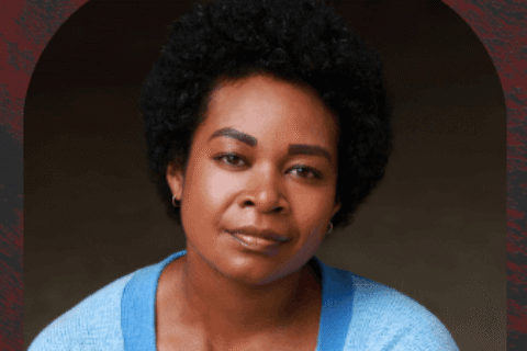 Photo of Emele Ugavule. Emele wears a blue cardigan. The background is grey.